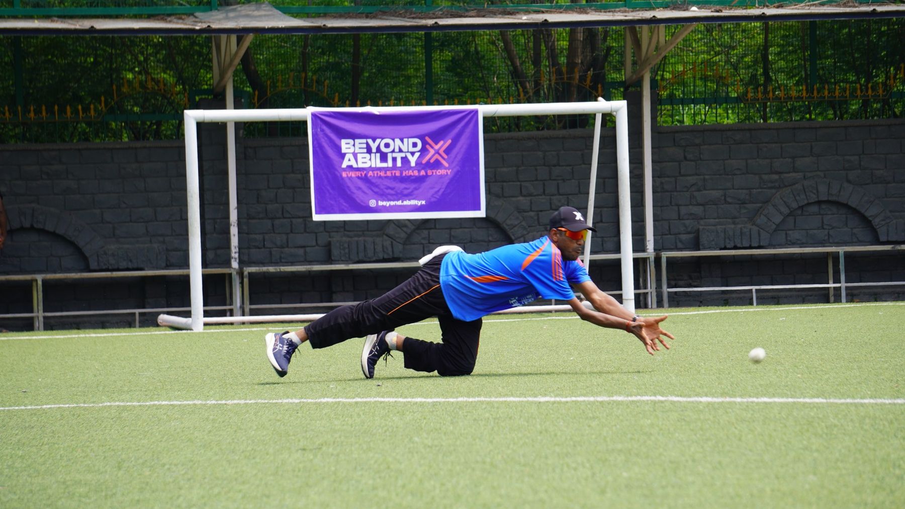 Ravindra Sante diving for a catch in front of a Beyond Ability X banner